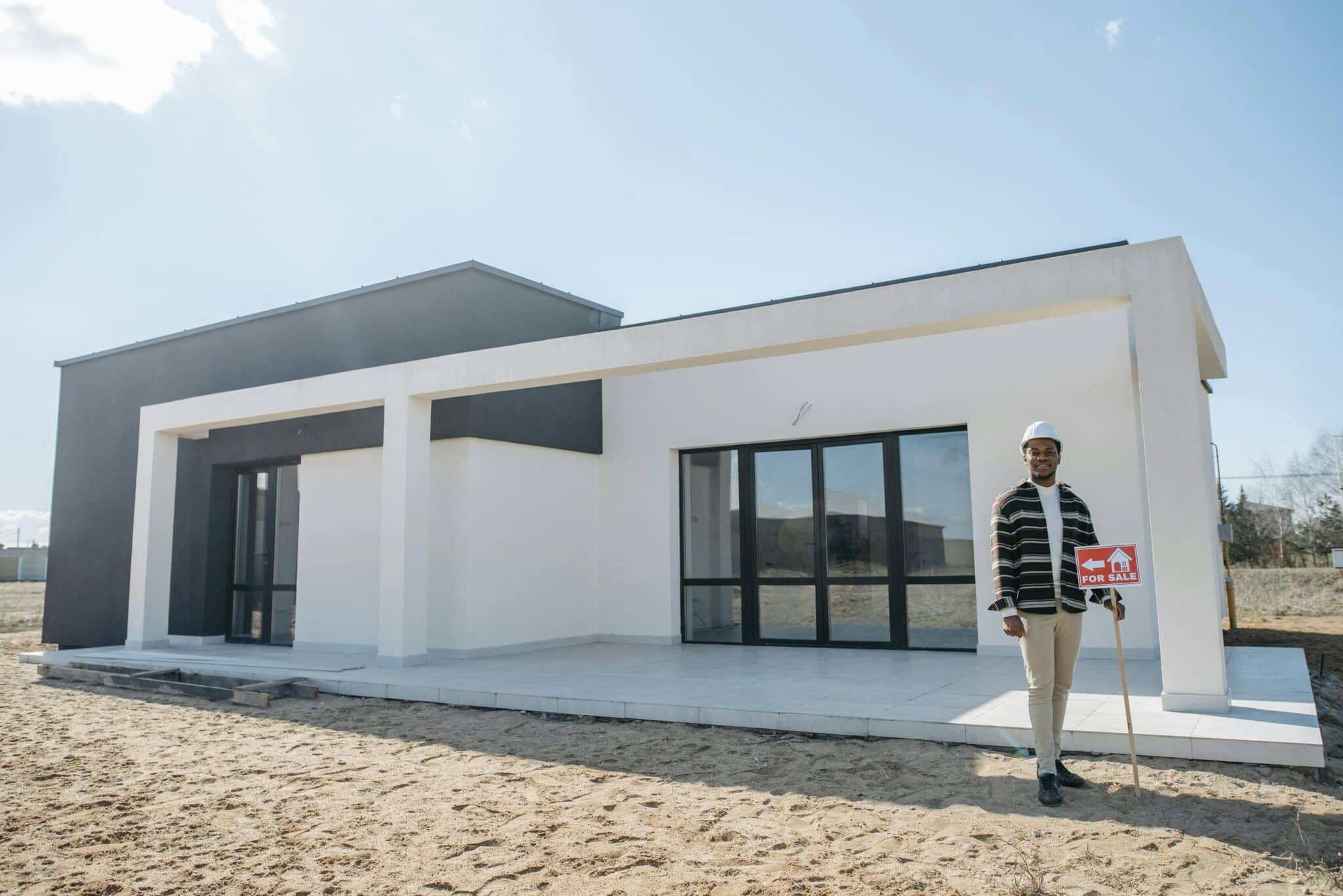 A man stands in front of a house with a sign, representing a Billings Realtor promoting a property for sale.