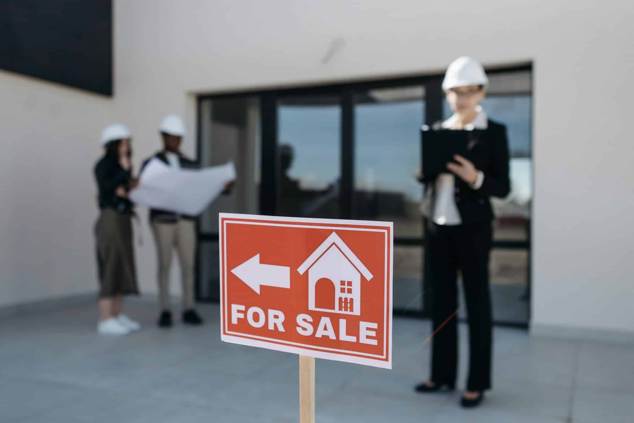 A man and woman stand by a for sale sign, representing Montana Real Estate Agents ready to assist buyers.